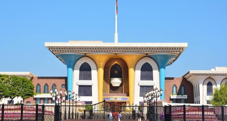 Un palacio colorido con una bandera omaní en la parte superior, cielo azul claro de fondo.