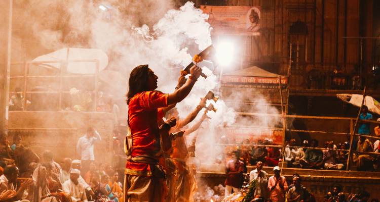 Silhouettes of people performing a river ceremony with smoke.
