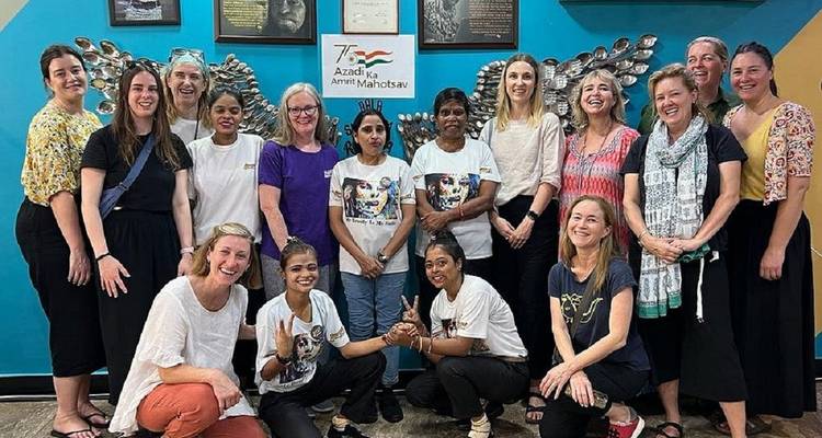 Large group of travellers and local women posing together inside a community centre.