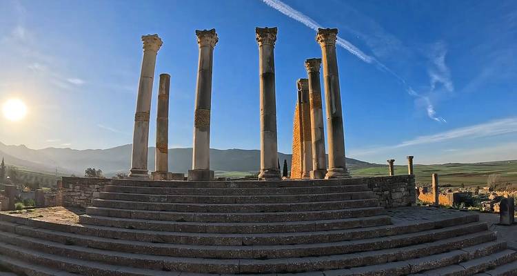 Rij antieke Romeinse zuilen bovenop stenen treden in open landschap met laag ochtendlicht en bergen in de verte