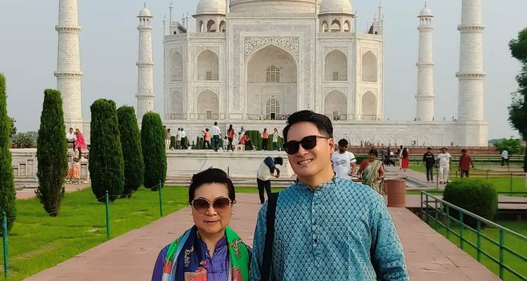 Two people posing in front of the Taj Mahal on a sunny day.