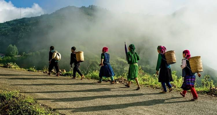 Dorpsbewoners uit etnische minderheden in kleurrijke kleding en met manden lopen over een mistige bergweg.