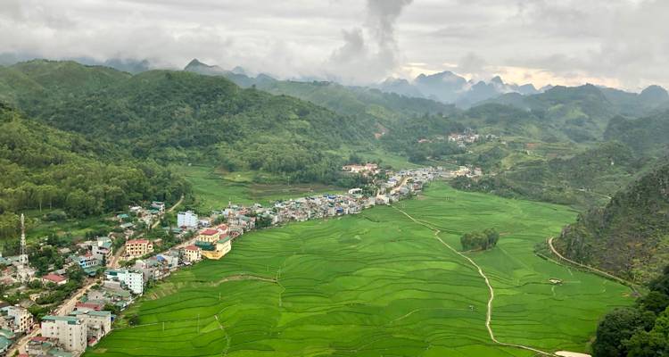 Uitzicht op een slingerende dalstad omringd door levendige groene terrasvormige heuvels onder bewolkte luchten