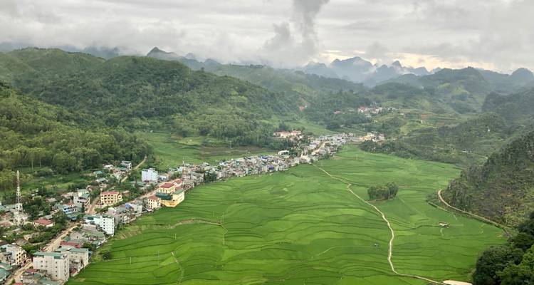 Luftaufnahme einer kleinen Stadt, die von üppigen terrassierten Reisfeldern und fernen Hügeln umgeben ist