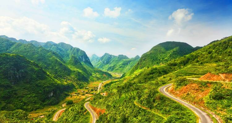 Helder panoramisch uitzicht op een groene vallei en slingerende geasfalteerde weg onder een heldere blauwe hemel.