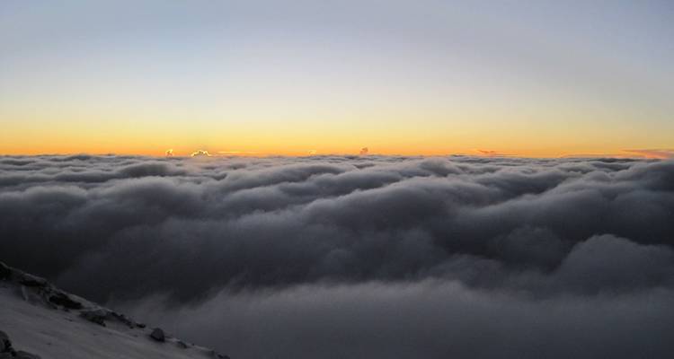 Wolken bei Sonnenuntergang über einer bergigen Landschaft.