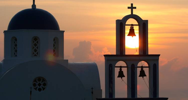 Silhouette d'une église avec des cloches et un dôme au coucher du soleil.