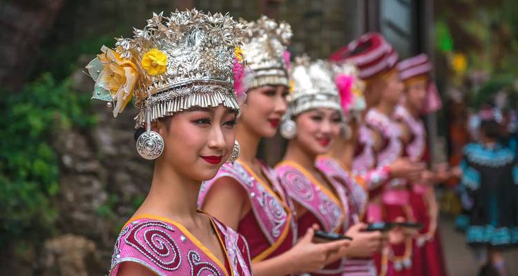 Rij van vrouwen van de Miao-minderheid in prachtige zilveren hoofddeksels en kleurrijke traditionele kleding die kopjes vasthouden voor een welkomstceremonie.