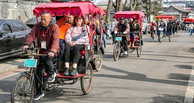 Stoet van bakfietsen met toeristen door bomenrijke straten in Pekings hutong-wijk.