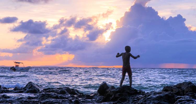 Enfant jouant sur des rochers sur une plage éclairée par le coucher de soleil.