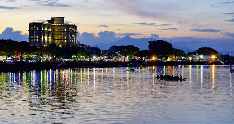Lumières de la ville se reflétant sur l'eau le soir avec un bâtiment au loin.