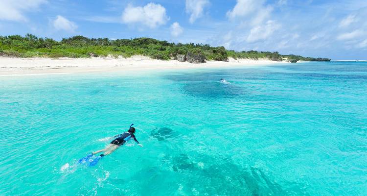 Snorkelaar die boven kristalhelder turkooiswater glijdt dicht bij een ongerepte wit zandstrand