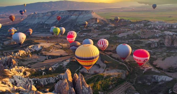 Hot air balloons over rocky landscapes at sunset.
