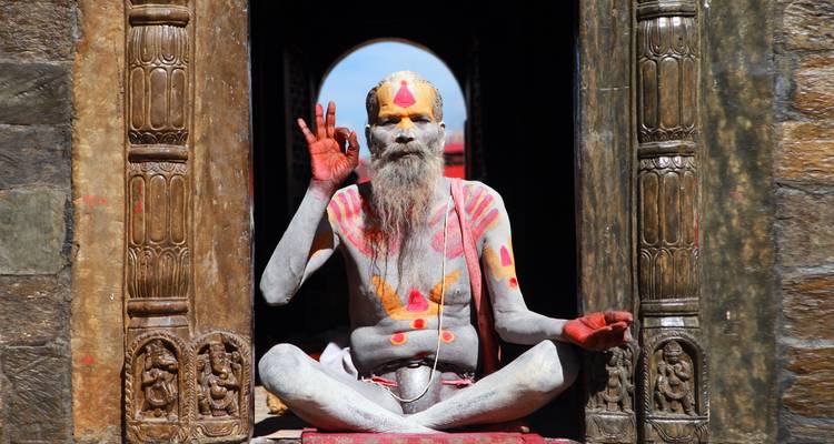 Bemalter Sadhu, der in einem Tempeltüreingang sitzt.