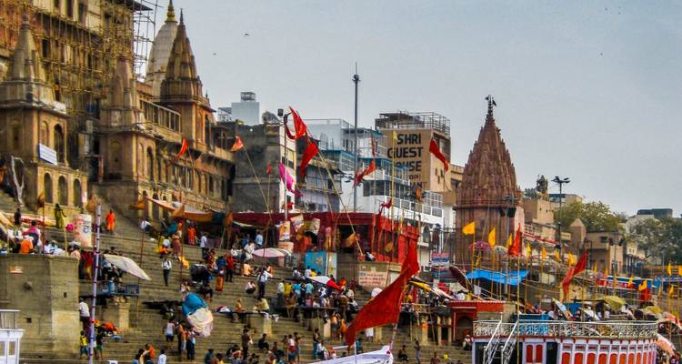 Belebte Ghats mit Menschen und Flaggen entlang des Flusses in Varanasi.