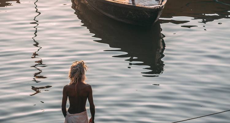 Person, die bei Sonnenuntergang im Wasser neben einem Boot steht.