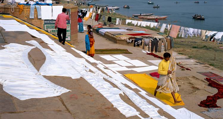Wäsche trocknet am Flussufer, während Menschen vorbeigehen.