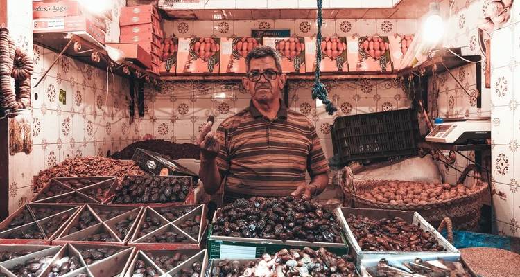 Étal de marché avec un vendeur et diverses dattes exposées.