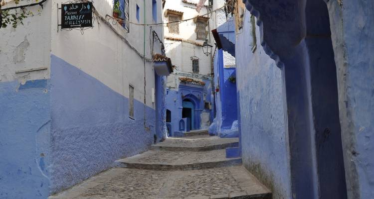 Une ruelle étroite pavée de galets avec des bâtiments peints en bleu.