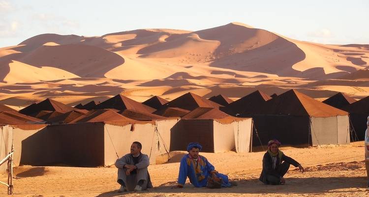 Des gens assis près de tentes du désert avec des dunes de sable.