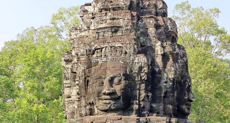 Ancien visage de pierre du temple du Bayon entouré de verdure.