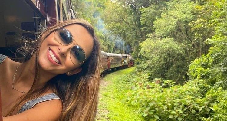 Person smiling from a moving train passing through lush greenery.