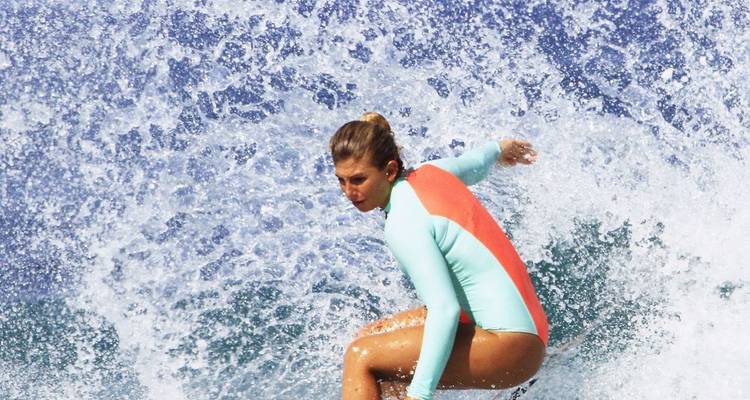 Female surfer catching a wave in vibrant blue water.