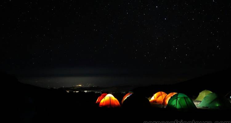 Les tentes colorées brillent sous un ciel étoilé sur les pentes du Kilimandjaro la nuit.