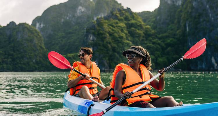 Deux touristes vêtus de gilets de sauvetage pagaient dans un kayak bleu à travers une eau émeraude entourée de pics calcaires.