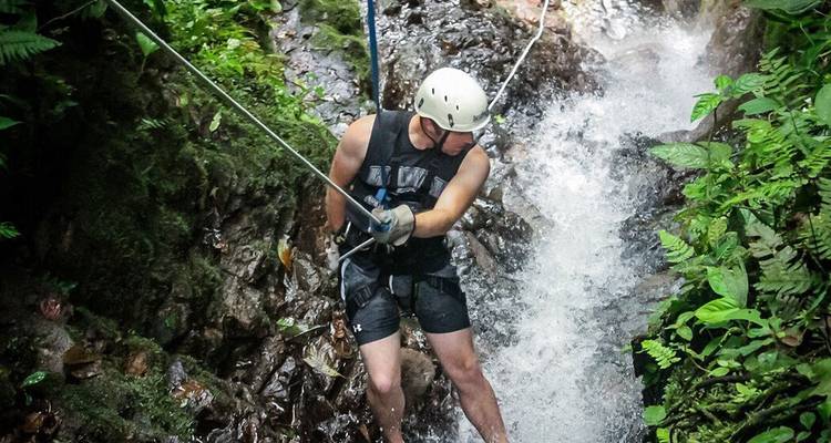 Un aventurero se deja caer por una cuerda a través de un canal de cascada rocoso mientras lleva puesto un casco.