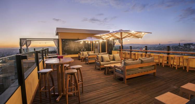 Une terrasse sur le toit avec des sièges et une vue panoramique sur la ville au coucher du soleil.