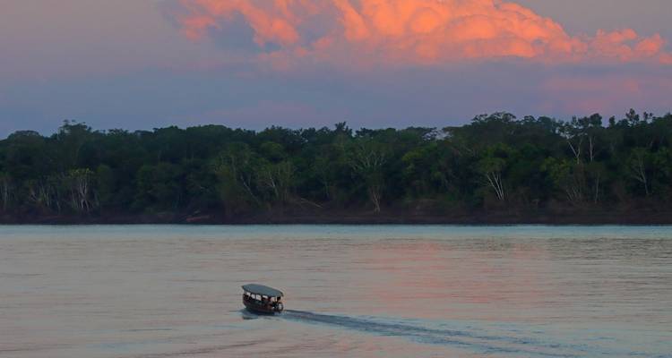 Barco navegando en un río durante el atardecer con orilla boscosa.