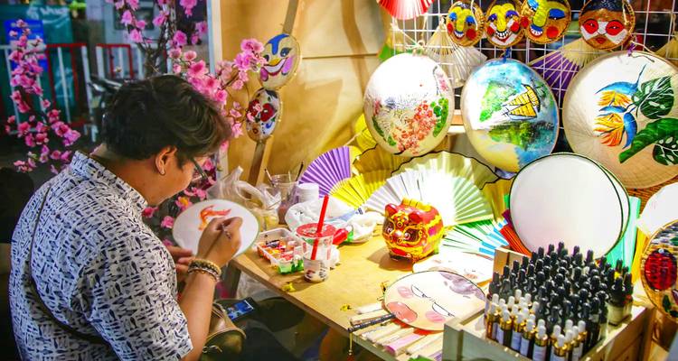 Ein Künstler, der auf traditionellem vietnamesischem Kunsthandwerk an einem Marktstand malt.