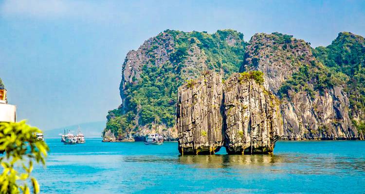 Ikonische Kalksteininseln in der Halong-Bucht mit Booten im Wasser.