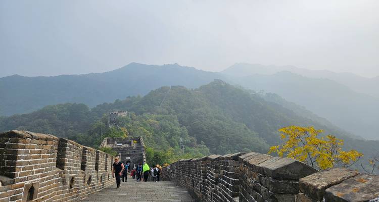 Visitors walking along a stone section of the Great Wall with misty mountains beyond