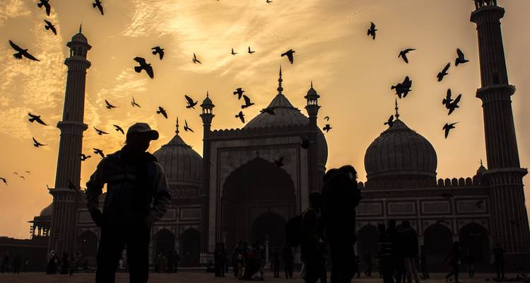 Silueta de personas y una mezquita con pájaros volando.