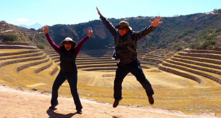 Zwei Menschen springen fröhlich vor antiken Terrassen.