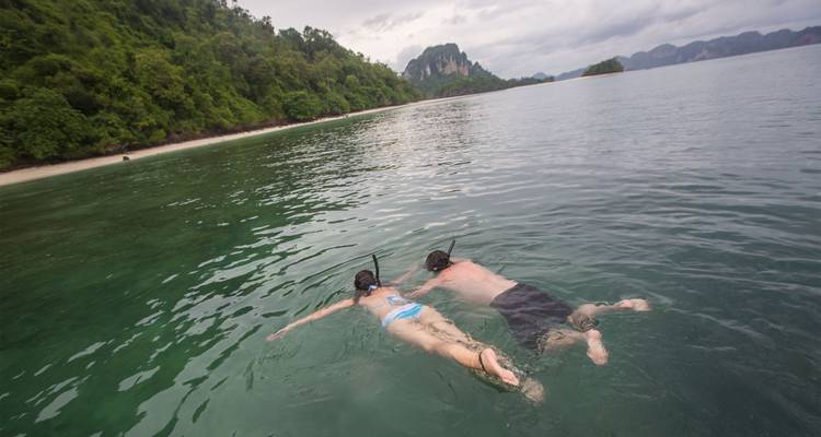 Mann und Frau schnorcheln nebeneinander in klarem Küstenwasser in der Nähe einer bewaldeten Uferlinie.