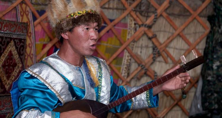 Mongoolse muzikant in traditionele kledij die een snaarinstrument speelt in een versierde ger.