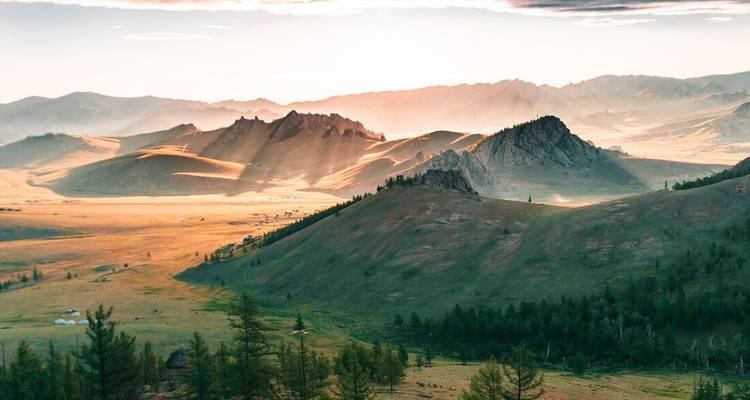 Gouden zonsopgang die lange stralen werpt over golvende steppen bezaaid met rotsige uitsteeksels en verre bergen.