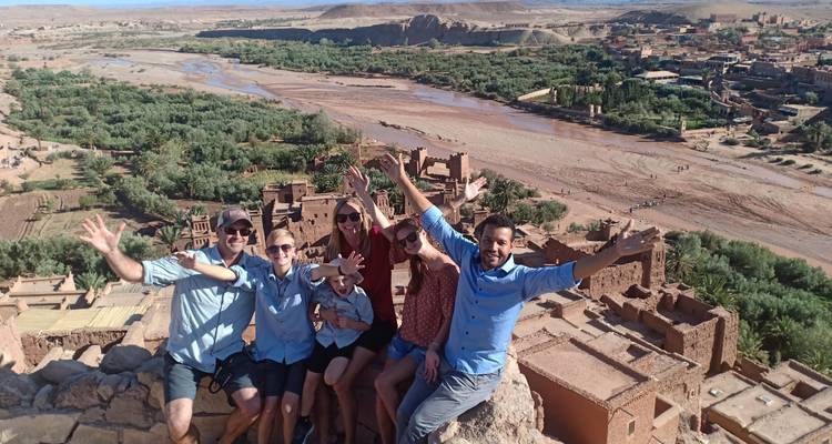 Groupe de touristes posant sur une colline pittoresque avec des structures anciennes en contrebas.