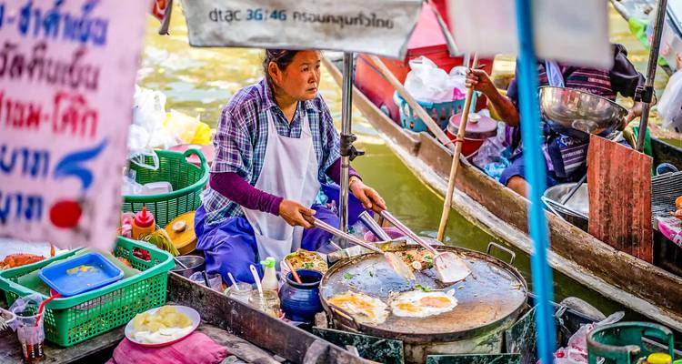 Vendedor de mercado flotante preparando comida en un barco rodeado de letreros coloridos.