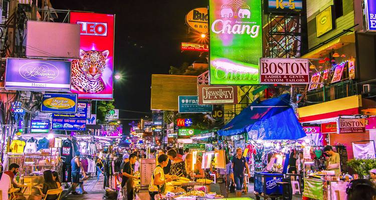 Mercado nocturno bullicioso con letreros de neón brillantes y numerosos peatones.