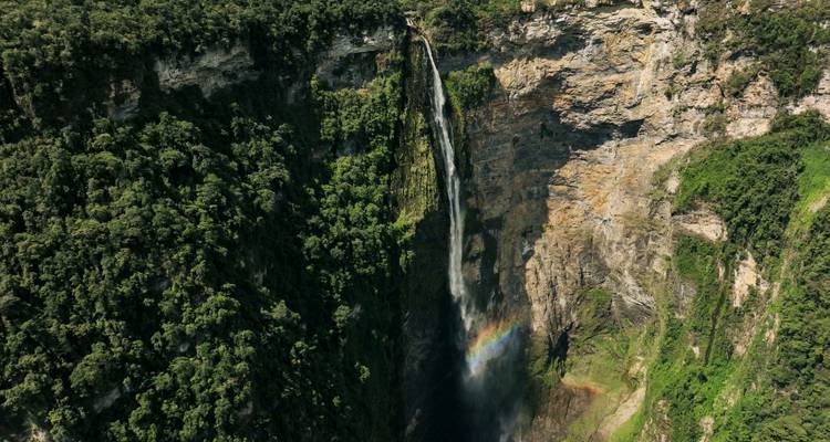 A tall waterfall with a rainbow, surrounded by cliffs.