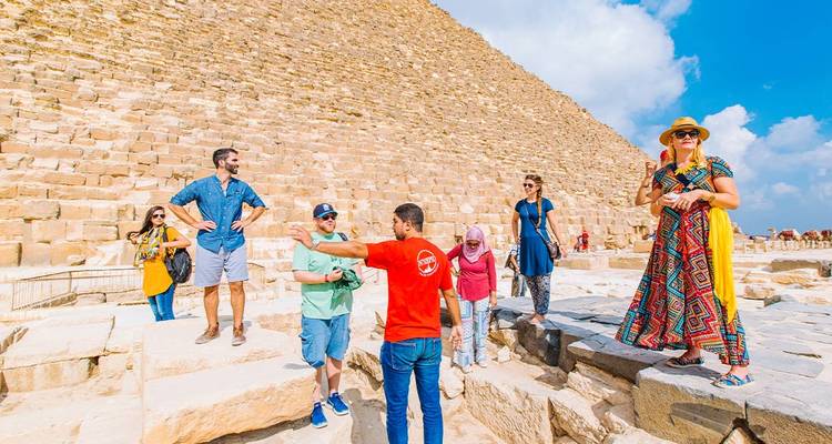 Guide expliquant la zone de la Grande Pyramide à un groupe de touristes debout sur des blocs de calcaire