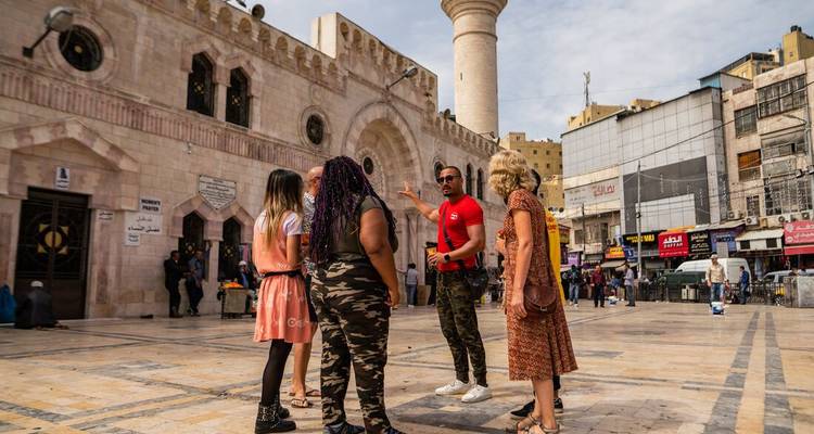 Touristes écoutant un guide devant une mosquée sur une place urbaine avec des boutiques