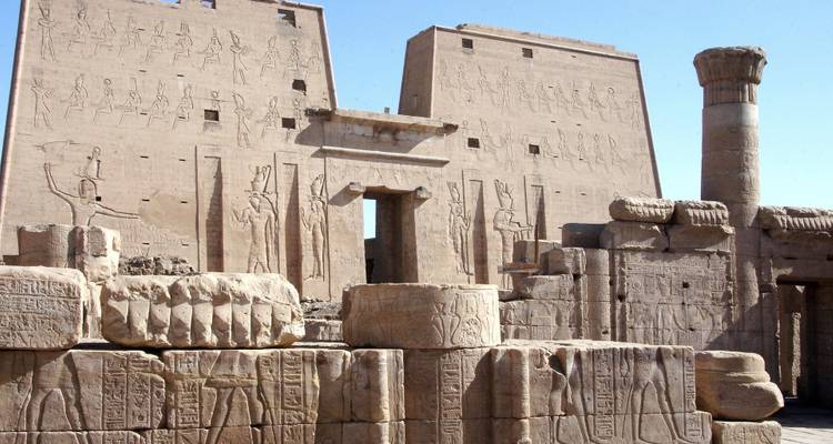 Sand-colored pylons and relief carvings of an ancient Egyptian temple complex under clear sky