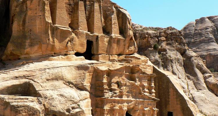 Rock-cut tomb facades and steps carved into golden cliffs at Petra under bright sky