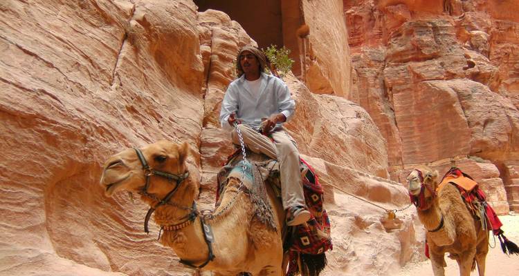 Man riding a camel through the rose-red sandstone gorge of Petra’s Siq