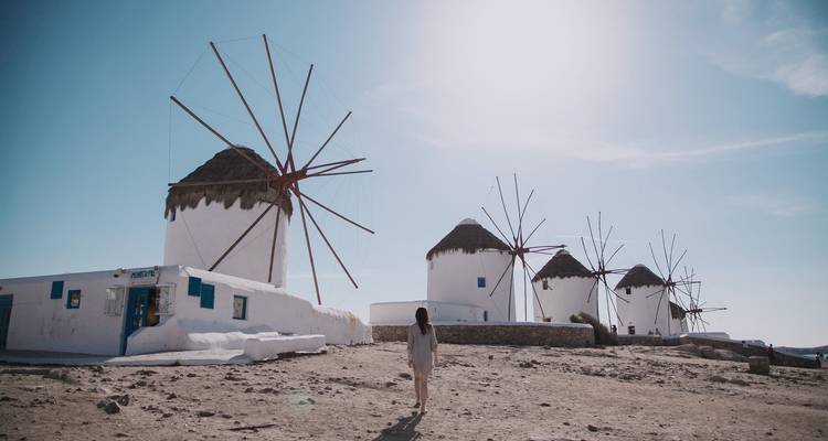 Iconic windmills on a sunlit island with a person walking towards them.